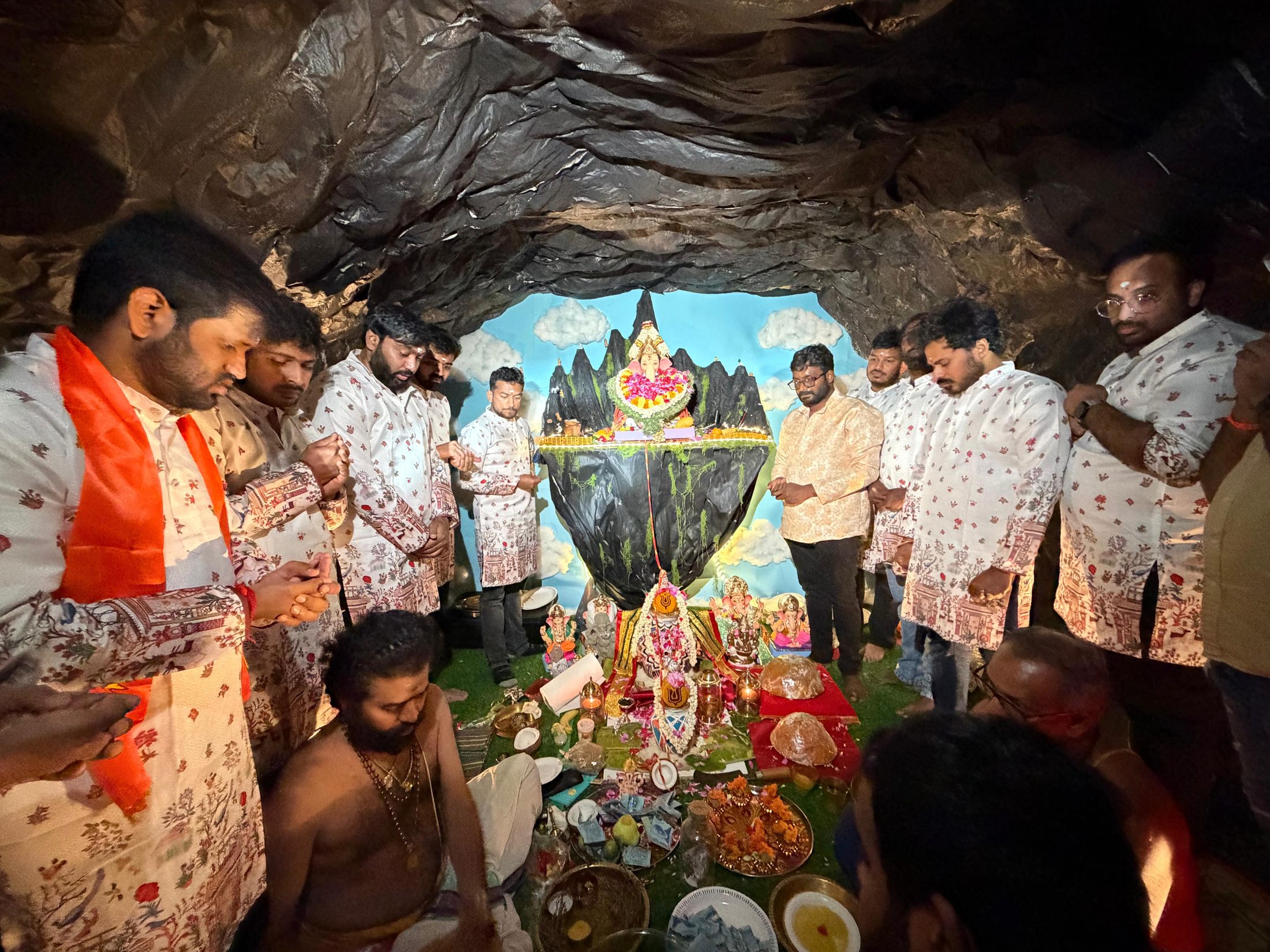 Devotees in white kurtas praying before Ganesha on a floating mountain inside our handmade cave set